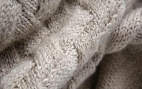 Tessuto a maglia grossa color crema, con un motivo a trecce che ricorda la morbidezza della flanella.