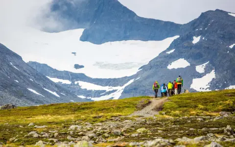 Vandrare med ryggsäckar går längs en stig med glaciärklädda sylarna runt.