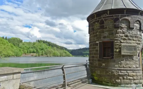 Ein schöner Tag zum spazieren gehen am NRW See. Ein alter Turm steht am Ufer, umgeben von grünen Hügeln und einem ruhigen See.