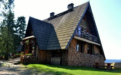 Drewniana bacówka na Turbaczu, z kamiennymi schodami i stosem drewna. Stare wierchy zapraszają do odpoczynku.