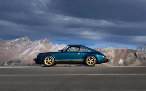 Ein türkisfarbener Porsche 911 SC mit goldenen Felgen und Streifen steht auf einer Bergstraße. Die Wertentwicklung dieses Klassikers ist beeindruckend.