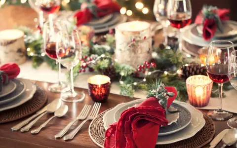 Tavola apparecchiata per un magico pranzo di Natale, con candele, pigne e luci scintillanti. Dove andare per un'atmosfera così?