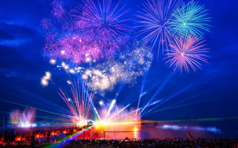 Spektakuläres Feuerwerk und Lichtshow an der Ostsee. Menschen feiern Silvester mit einer ausgelassenen Party am Strand.