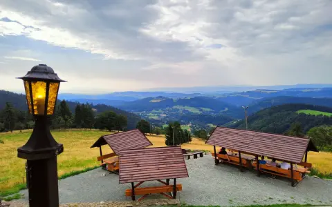 Widok z **schroniska górskiego Orzeł** na malownicze wzgórza. Wiaty z ławami i stołami zapraszają do odpoczynku.