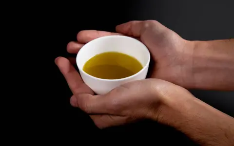 Mani che sorreggono una tazzina bianca con olio extravergine di oliva dorato. Un gesto per imparare come riconoscere olio extravergine di oliva.