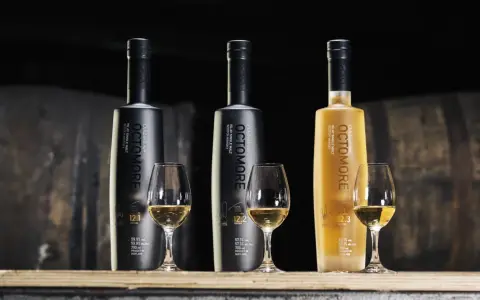 Trzy butelki Octomore, znanej z tego, że jest najbardziej dymna whisky, stoją obok kieliszków z bursztynowym płynem.