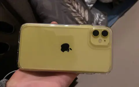 Żółty iPhone 11 w przezroczystym etui, trzymany w dłoni.