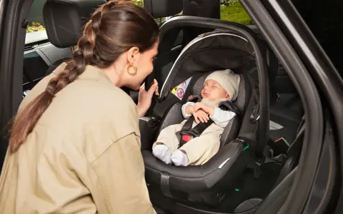 Madre mira a su bebé dormido en la silla coche, asegurando la correcta postura recien nacido silla coche para un viaje seguro.