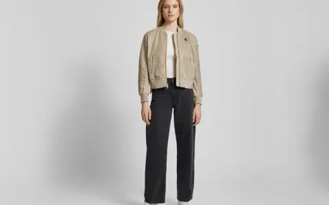 Frau stylt eine beige Bomberjacke mit weiten schwarzen Jeans und weißen Sneakern. Ein lässiger Look, der sich leicht anpassen lässt.