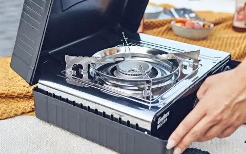 Tragbarer Gaskocher mit offenem Deckel, bereit für die Zubereitung von Speisen. Die Gaskartuschen lagern sicher im Inneren.
