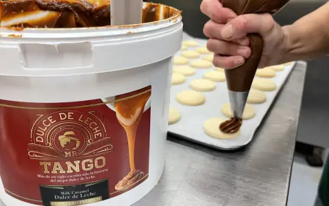 Un repostero usa una manga pastelera para decorar galletas con dulce de leche, mostrando cómo hacer dulce de leche.