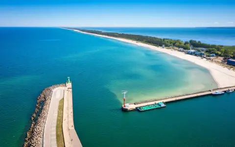 Władysławowo miasto, port z falochronem i latarnią morską, na tle piaszczystej plaży i turkusowego morza.