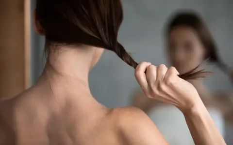 Kobieta w lustrze skręca włosy, myśląc o domowej odżywce z wody ryżowej dla ich wzmocnienia.