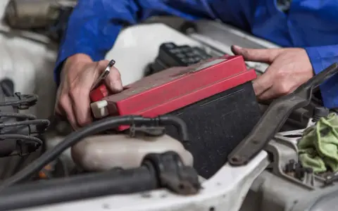 Mechanik wymienia akumulator w Peugeot 508. Widać ręce trzymające klucz i czerwony element akumulatora.