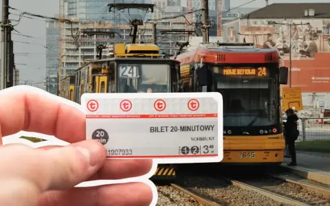 Warszawski bilet 20 minutowy w dłoni, na tle tramwajów i miejskiej zabudowy.