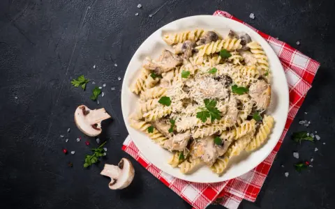 Pyszny makaron z kurczakiem i pieczarkami w kremowym sosie, posypany parmezanem i świeżą pietruszką.