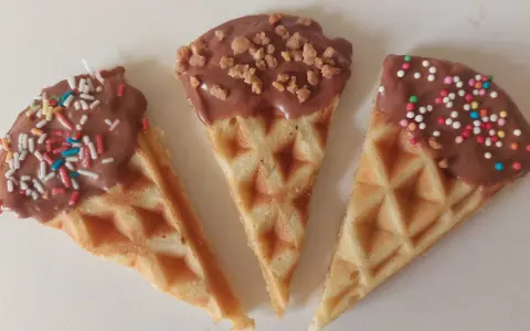 Drei dreieckige Waffeln, mit Schokolade überzogen und bunt bestreut, warten darauf, von Kindern beim Waffeln dekorieren vernascht zu werden.