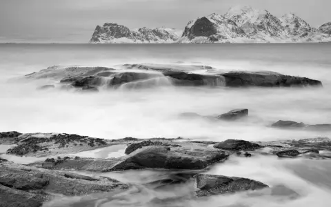 Vatten virvlar runt stenar vid en snötäckt kust. Perfekt för zoom fotoresor.