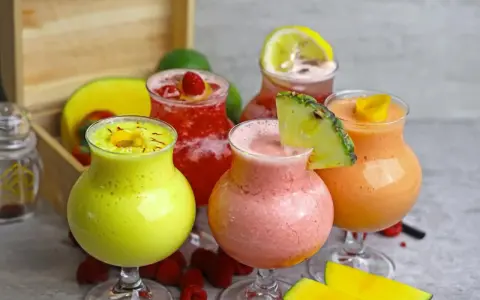 Cinq verres de boisson énergisante maison aux fruits colorés : jaune, rose, rouge et orange, garnie de fruits frais.