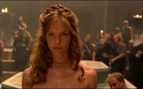 Die schöne Helena, Menelaos' Frau, blickt ernst in die Menge. Ihr Haar ist kunstvoll geflochten, ein goldenes Halsband schmückt ihren Hals.