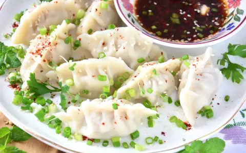 Pierożki gyoza, posypane szczypiorkiem i sezamem, podane z sosem.