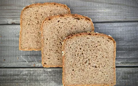 Drei Scheiben **Vollkornbrot** aus der **Kastenform** liegen auf rustikalem Holz.