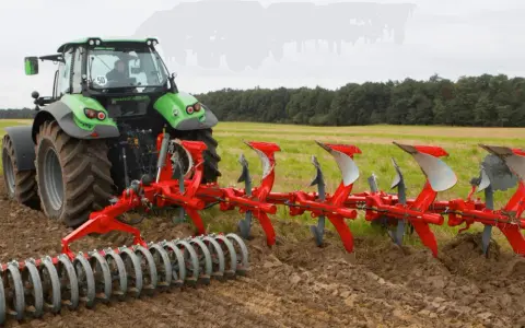 Zielony traktor z pługiem obrotowym pracuje na polu, przygotowując ziemię do siewu.