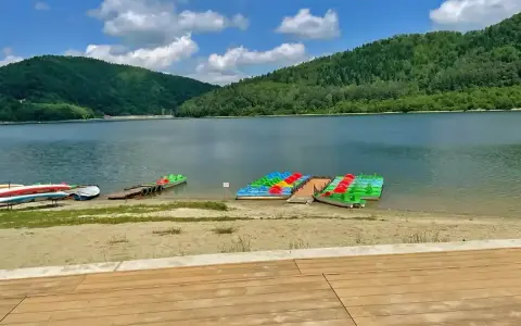 Jezioro Klimkowskie plaża z kolorowymi rowerami wodnymi i kajakami, otoczona zielonymi wzgórzami.