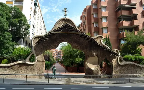 Portail organique, œuvre de Gaudí à Barcelone, avec une statue d'homme devant.