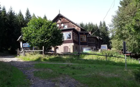 Drewniany budynek schroniska Sowa otoczony lasem. Przed nim zielony trawnik i droga.