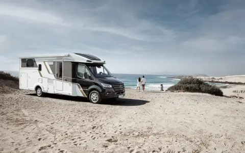 Eura Mobil husbil parkerad på en sandstrand vid havet. Ett par står och tittar ut över vågorna.