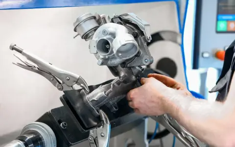 Mechanik pracuje nad turbosprężarką, mocując ją imadłem. Widoczny jest zawór N75, kluczowy element sterujący pracą turbiny.