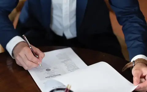 Mężczyzna w garniturze podpisuje dokument, składając oświadczenie woli.