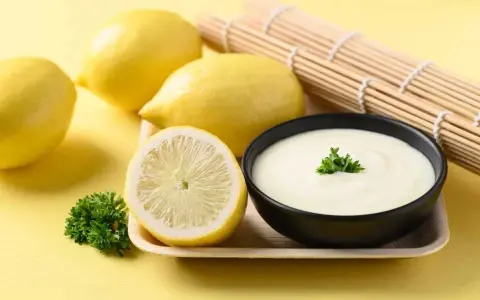 Un bol de sauce beurre citron crémeuse, garni de persil, avec des citrons frais et un rouleau de bambou en arrière-plan.
