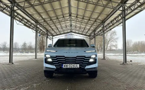Jasny Jetour Dashing z charakterystycznym grillem i światłami LED stoi pod zadaszeniem.