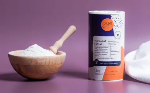 Holzschale mit weißem Konjakmehl und Löffel daneben, eine Dose mit der Aufschrift "Konjakmehl" und Produktinformationen.