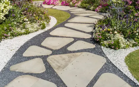 Ein geschwungener Weg aus unregelmäßigen Trittsteinen im Garten, umgeben von bunten Blumen und Kies. Perfekt, um Trittsteine Garten selber machen.