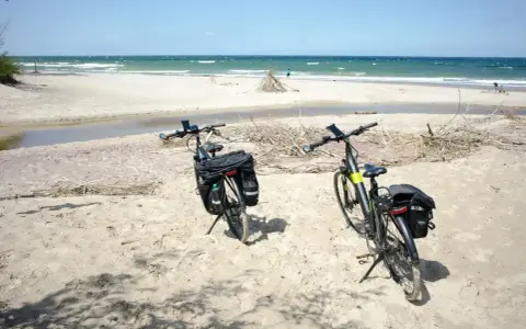 Dwa rowery z sakwami na piaszczystej plaży, gotowe na odkrywanie tras rowerowych nad morzem.