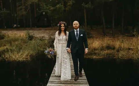 Para idzie przez las, ona w koronkowej sukni i wianku, on w garniturze. Ich suknia ślubna boho rustykalna idealnie pasuje do leśnej scenerii.
