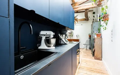 Cuisine moderne avec armoires bleues, évier noir et robot pâtissier. L'entrée de la maison donne directement dans cette pièce fonctionnelle et stylée.