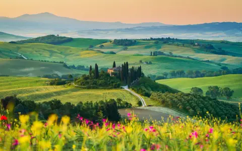 Un casale solitario su una collina, circondato da cipressi e dolci colline verdi, un sogno per un tour della Toscana.