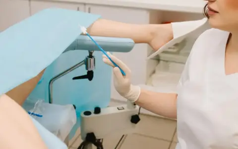 Lekarz przygotowuje się do gbs badanie, trzymając wymazówkę. Pacjentka leży na fotelu ginekologicznym.