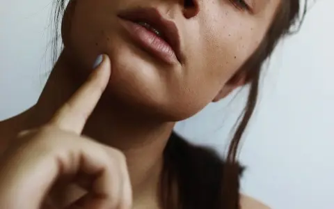 A woman's face, with a finger gently touching her cheek, suggesting a moment of self-care and a relaxing facial massage at home.