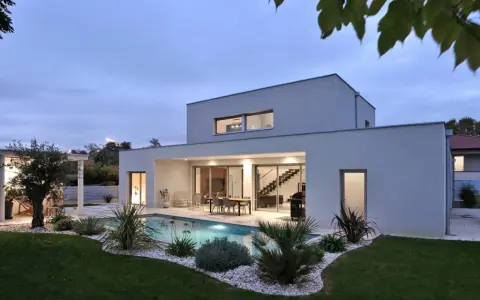 Vue arrière d'une maison moderne avec piscine illuminée, terrasse et jardin paysager. Un exemple de plan maison de luxe.