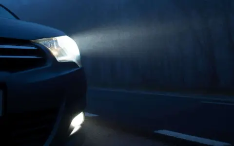 El alumbrado de posición de un coche ilumina la niebla en una carretera oscura.