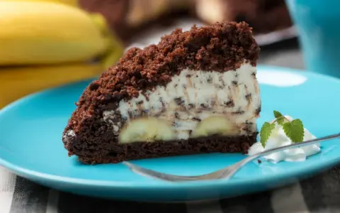 Ein Stück saftiger Maulwurfkuchen vom Blech mit Bananen und Schokostückchen in der Creme, garniert mit Sahne und Minze.