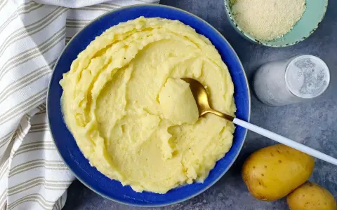 Un piatto di cremoso pure di patate, pronto per essere gustato. Accanto, patate fresche, sale e formaggio grattugiato.