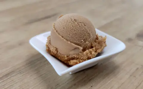 Eine Kugel cremiges Coca Cola Eis in einer weißen Schale auf Holzhintergrund.