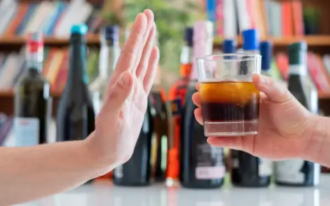 Dłoń odrzuca szklankę z alkoholem, symbolizując początek leczenia alkoholizmu.
