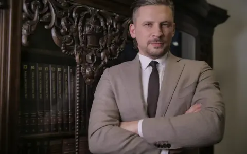 Mężczyzna w garniturze stoi na tle regału z książkami.